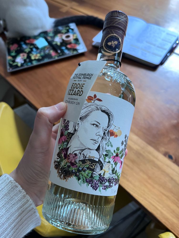 Bottle of EG Eddie Izzard gin featuring a label with a drawing of Suzy surrounded by the botanicals featured in the gin