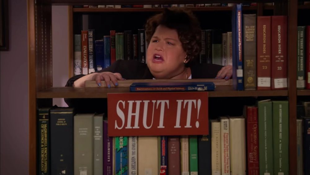 Laurie Beth Denberg as an angry librarian with a SHUT IT! sign