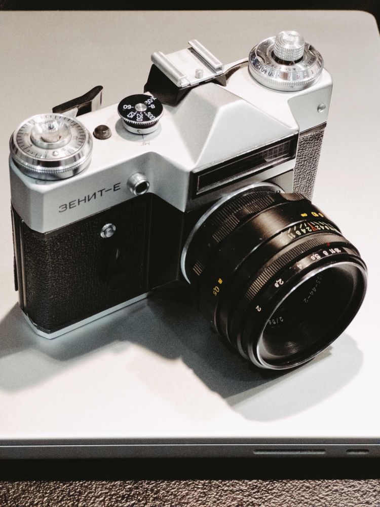 A Zenit E film camera photographed lying on top of a silver coloured laptop