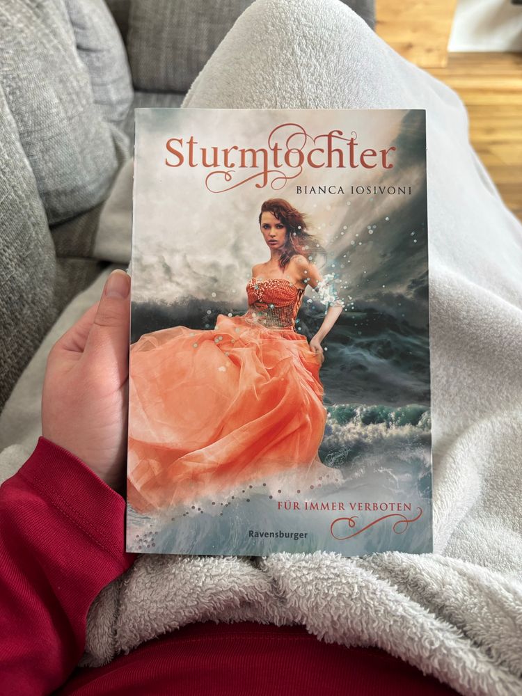 Ich halte das Buch „Sturmtochter - für immer verboten“ in der Hand. Auf dem Cover steht eine junge Frau in einem langen Kleid in tosendem Wasser.