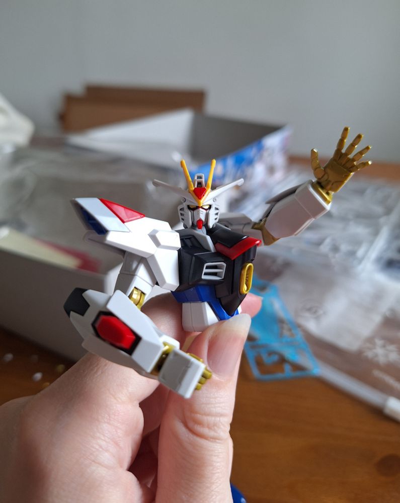 A picture of the HG Mighty Strike Freedom gunpla model kit partially assembled from the chest up. Posed waving at the camera.