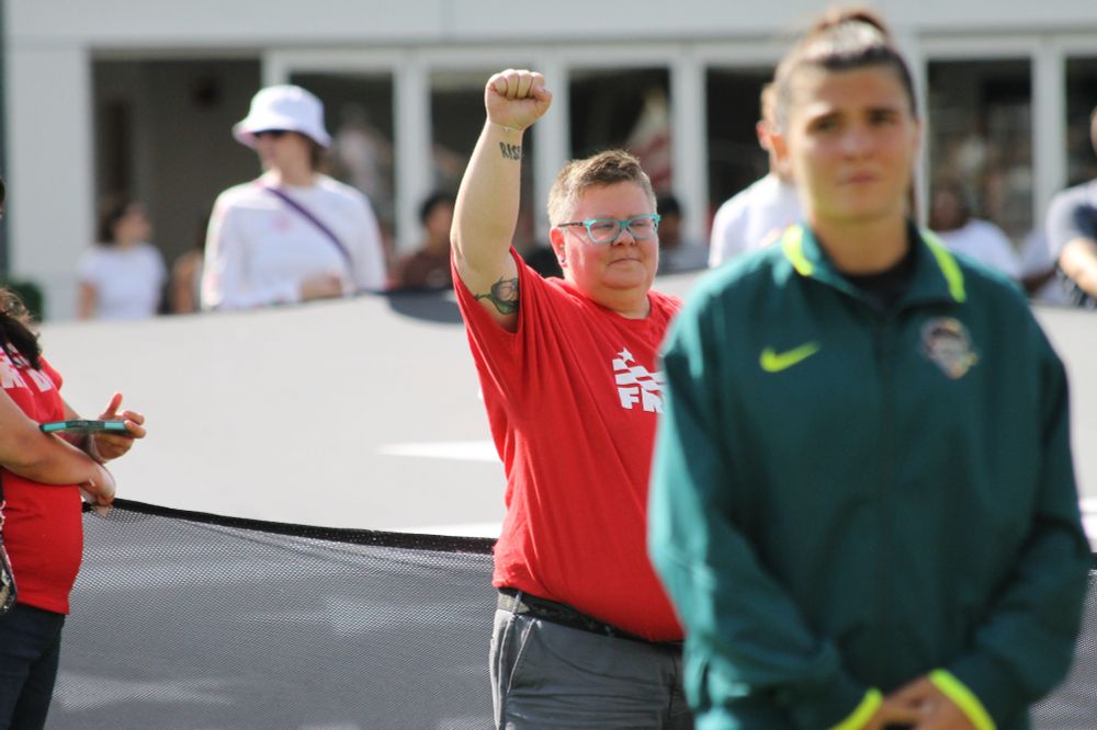 A fan holds up a fist while wearing a free DC shirt in the background as Washington Spirit player Sofia Cantore stands with her hands held at her waist in the foreground