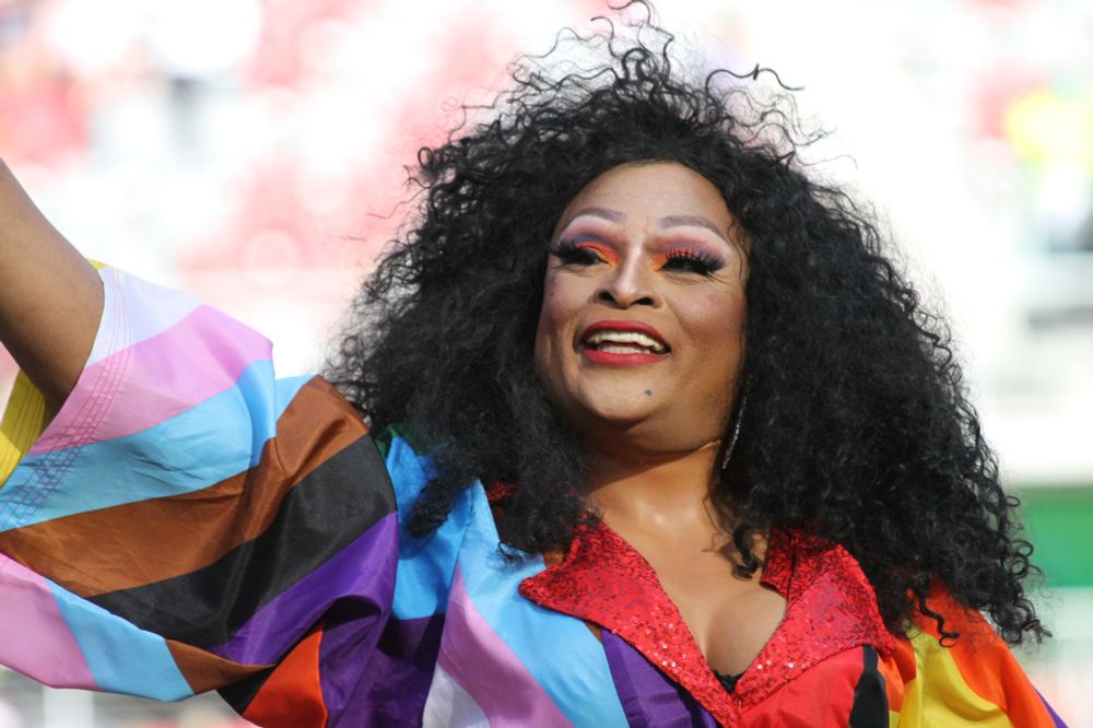 Drag queen Shi-Queeta Lee, in a dress made of pride flags, waves to the crowd during the halftime parade around the field for Pride Night