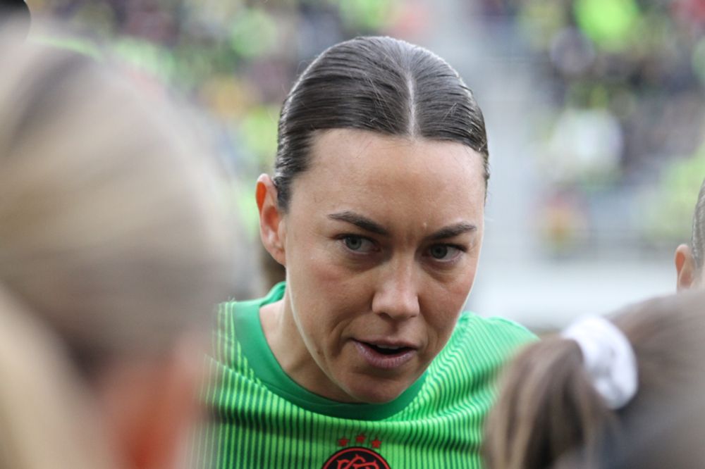 Mackenzie Arnold looking on during the pregame huddle. The top of her green goalkeeper jersey is visible