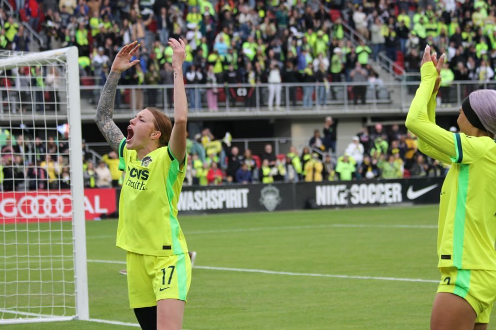 Hands all the way over her head, cheering toward the supporters section