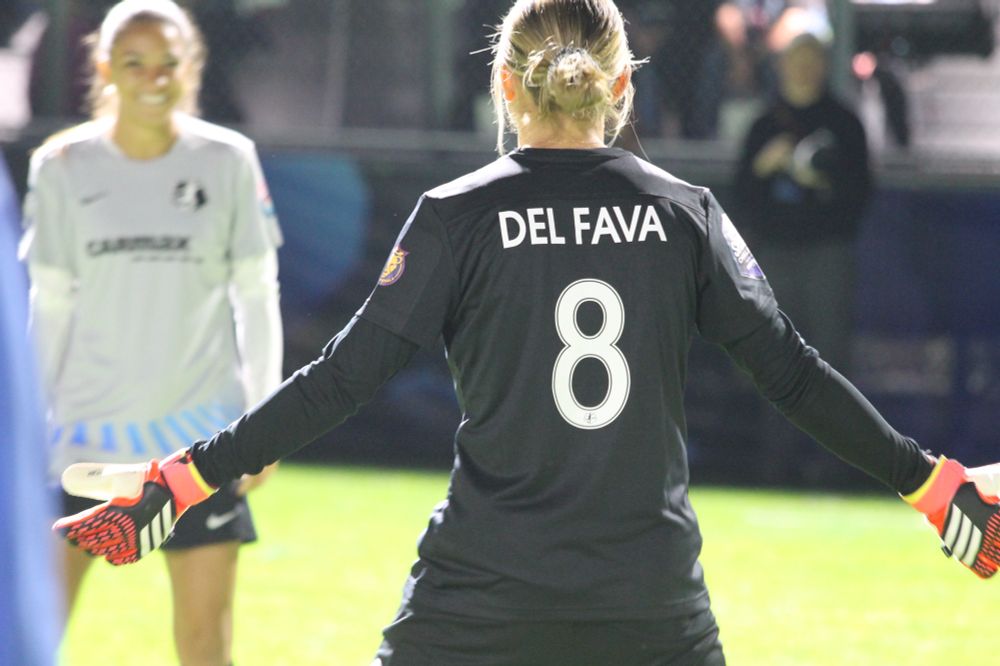 Kate Del Fava from behind in a black jersey, standing with her arms out and goalkeeper gloves on.