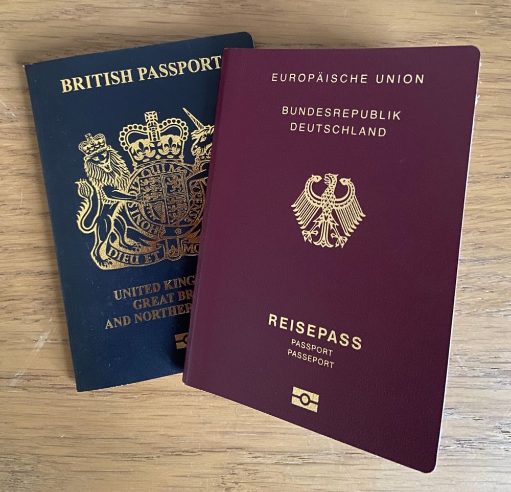 A dark blue British passport and a maroon red German passport lying next to each other 