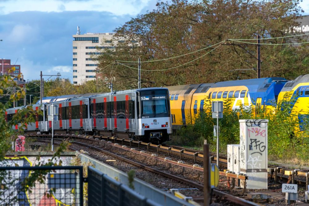Narrow silver metro train next to a yellow double decker train
