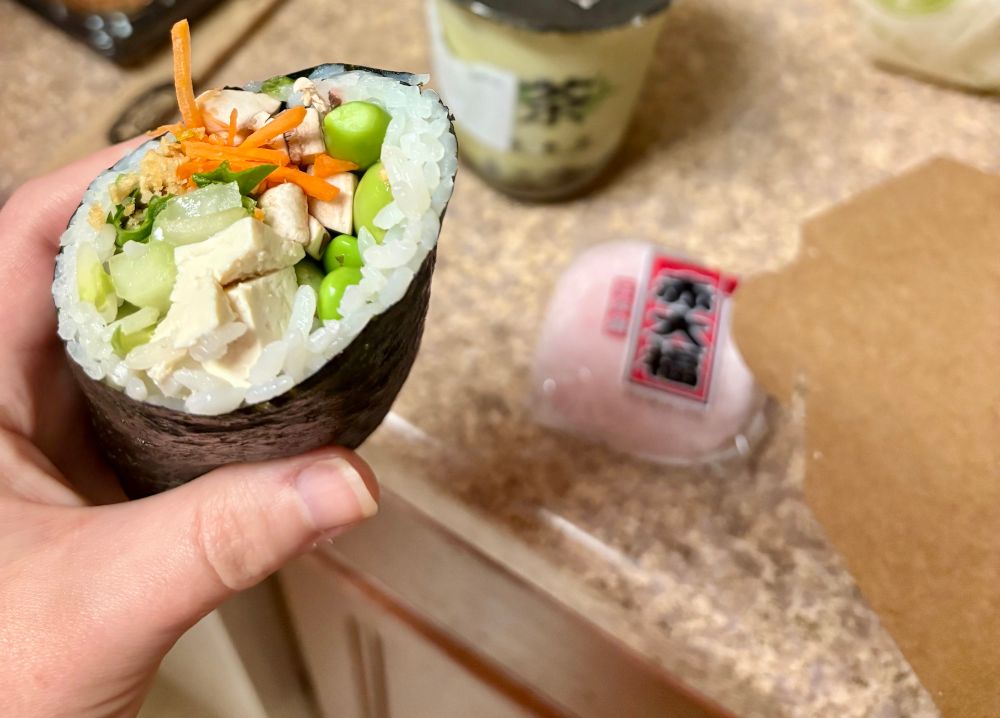 holding a large sushi “burrito” next to a matcha boba tea & strawberry daifuku