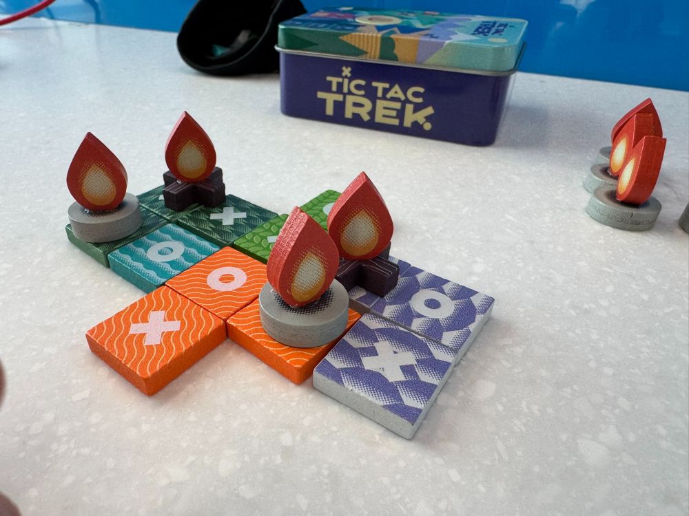tic tac trek in play on the recharging phones station. 

All painted wooden pieces. Small square tiles have terrain colors and an X or an O. Campfire pieces also have an X or an O base and are on top of some squares (where a 3 in a row was completed)