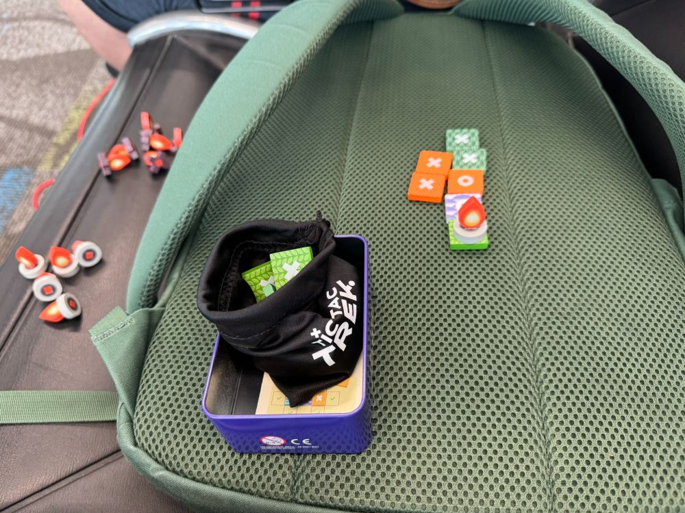 tic tac trek in play on the back of my backpack on the chair between me and on my opponent. 

All painted wooden pieces. Small square tiles have terrain colors and an X or an O. Campfire pieces also have an X or an O base and are on top of some squares (where a 3 in a row was completed)