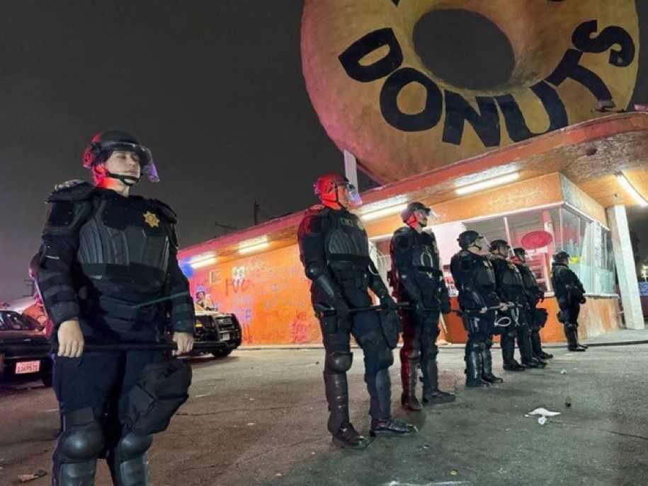 Stormtrooper-ass looking cops standing in front of a giant donut. 