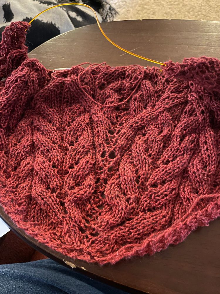 A red cable flare lace shawl, about half done, still on the needles