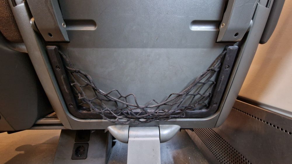 En ubrukelig oppbevaringslommen i ryggen på stolsetet foran på et tog pga gammel strikk uten elastisitet. 