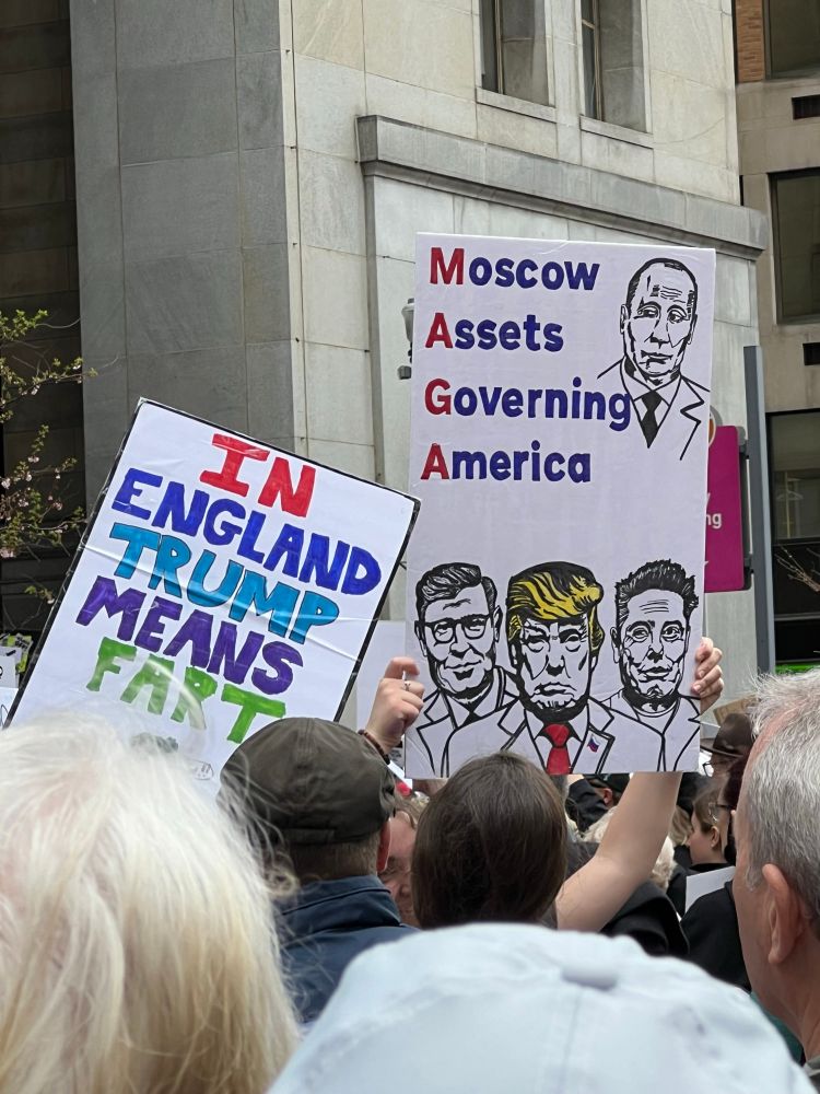 Protest signs pictured, the first one says “in England trump means fart” and the second one features a drawing of trump, musk and (I think) Johnson and says “Moscow Assets Governing America” with the MAGA in the words highlighted down the side  