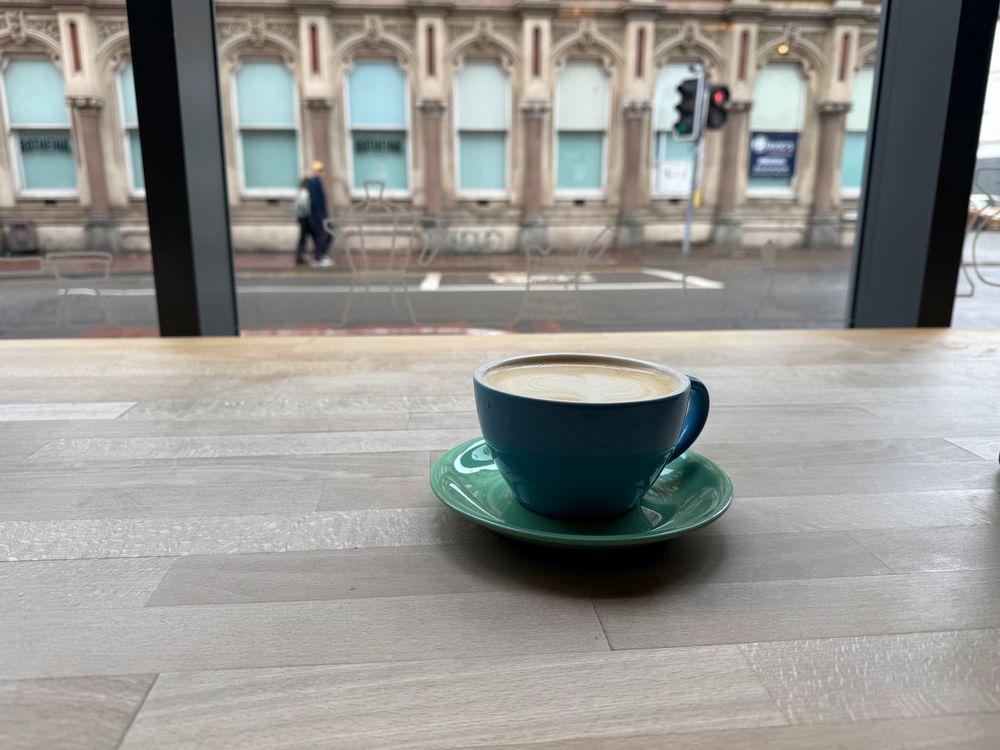 A cup of oat latte on a table looking out the café window in Cardiff Bay. 