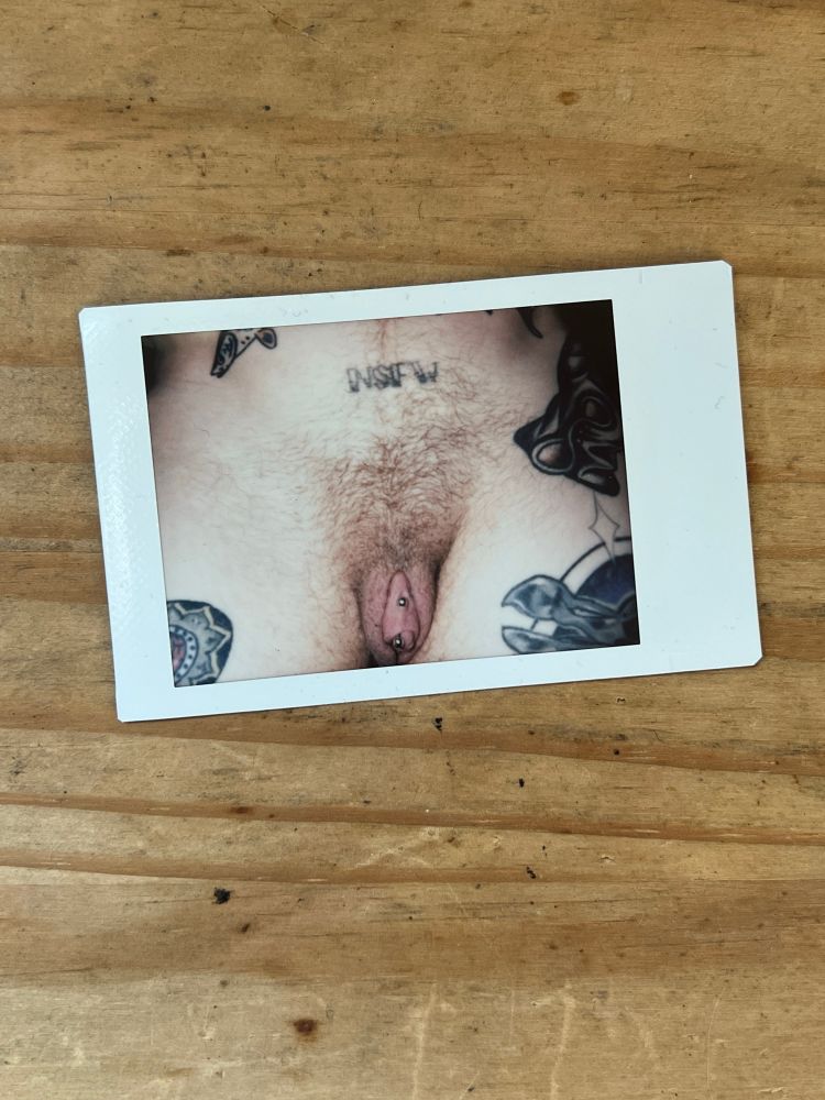 Instax print of pierced ftm cock. The print is on a wooden table. 