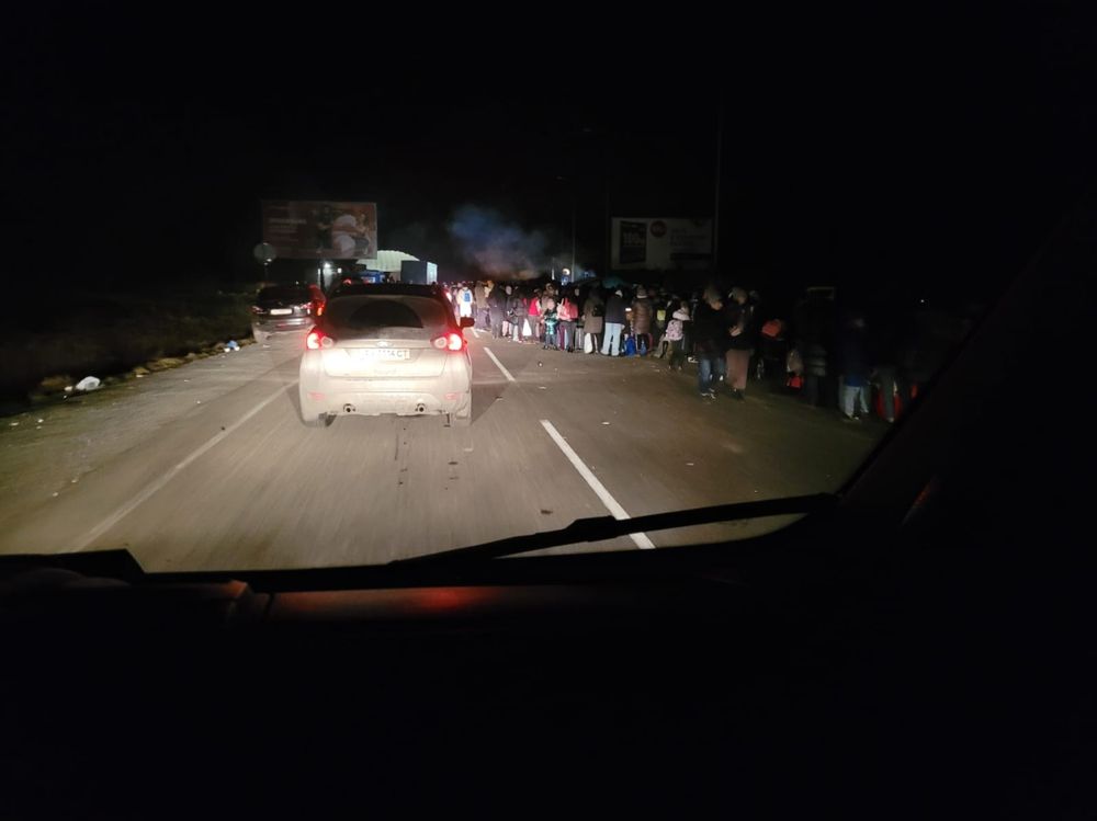Es ist Nachts, Menschen drängen sich in langen Reihen auf der Fahrbahn, links und rechts verlassene Autos. Im Hintergrund Rauch, welcher von nicht erkennbaren "Ghetto Tonnen" aufsteigt.
