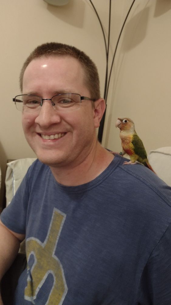 Picture of green cheeked conure sitting on my shoulder as I smile at the camera.