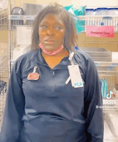 a woman wearing a mask and a name tag is standing in front of a pink sign that says personal care .