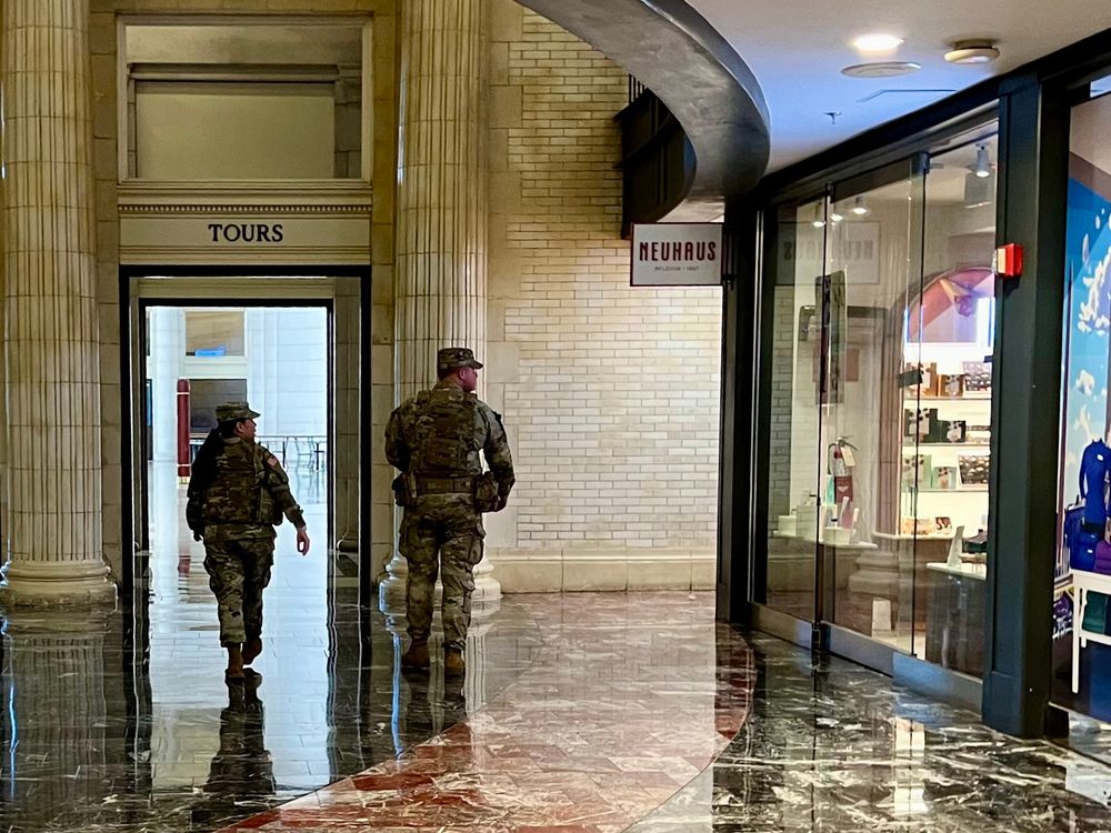 A young man and a young women in khaki camouflage uniforms glance into a luxury chocolatier shop in Union Station in Washington DC as they walk past. A 