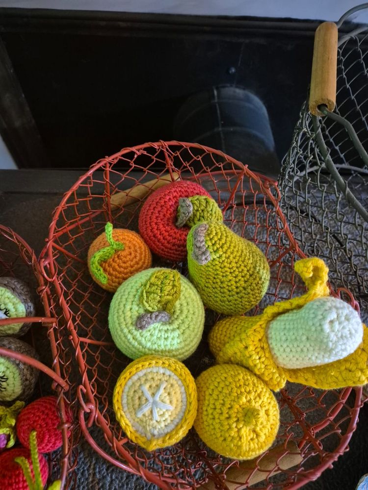 Panier en métal rouge contenant les fruits suivants en crochet : une pomme rouge, une orange, une pomme verte, un citron, une tranche de citron, une banane mi épluchée. On devine à côté un autre panier rouge contenant d'autres fruits en crochet.