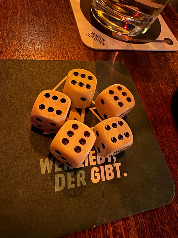 Auf dem Bild sieht man fünf Würfel, die auf einem dunklen Untersetzer liegen. Alle Würfel zeigen die Zahl sechs nach oben. Die Würfel sind elfenbeinfarben mit schwarzen Augen.

Der Untersetzer hat weiße Schrift, auf der teilweise zu lesen ist: „WER LIEBT, DER GIBT.“ Im Hintergrund erkennt man eine Holzoberfläche, darauf ein Glas mit Getränk, das auf einem weiteren Bierdeckel steht. Die Szene wurde im EISEN aufgenommen, der weltschönsten Kneipe in Bremen.