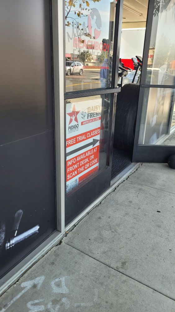 Photo of a doorway entrance to a small gym in Southern California. The sign in focus is one advertising "Daisy Fresh American Jiu-jitsu/Pedigo Submission fighting" and their trial classes