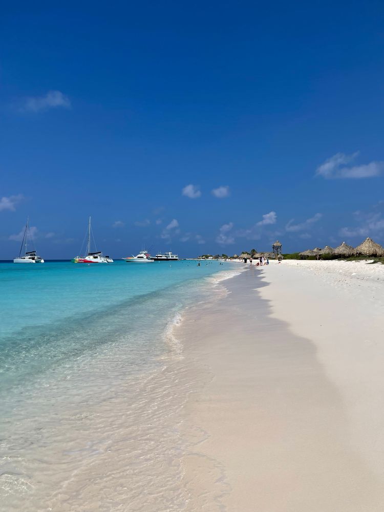 White sandy beach with beautiful turquoise ocean and sail boats on Klein Curaçao. 