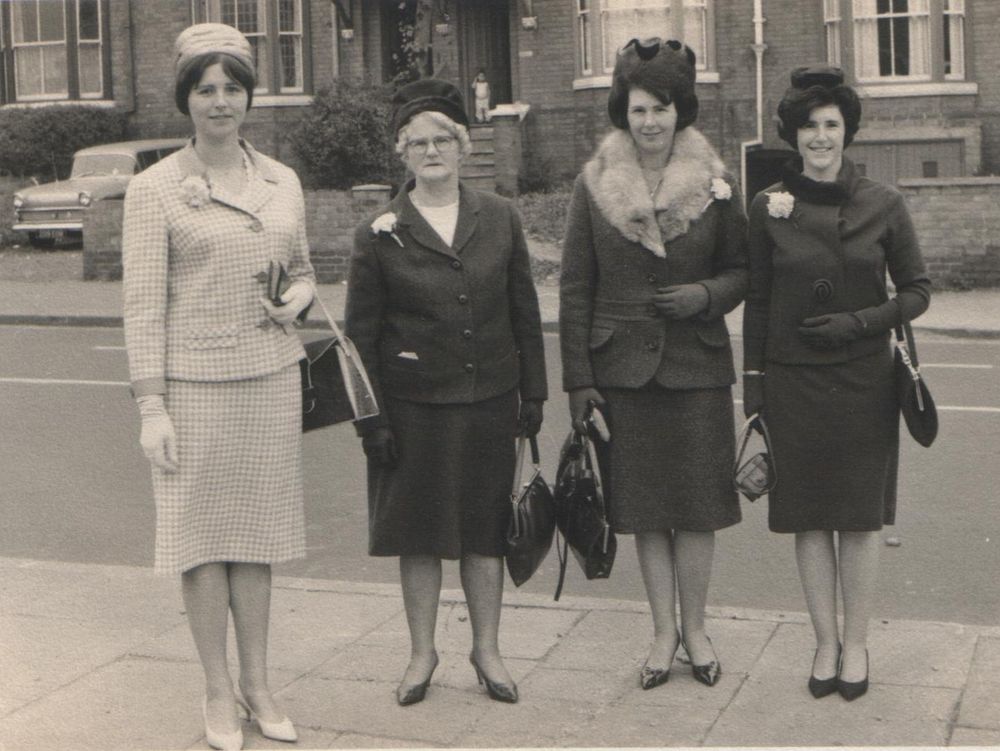 An older lady and her daughters dressed in suits and hats for a wedding pose on a victorian street, circa 1959