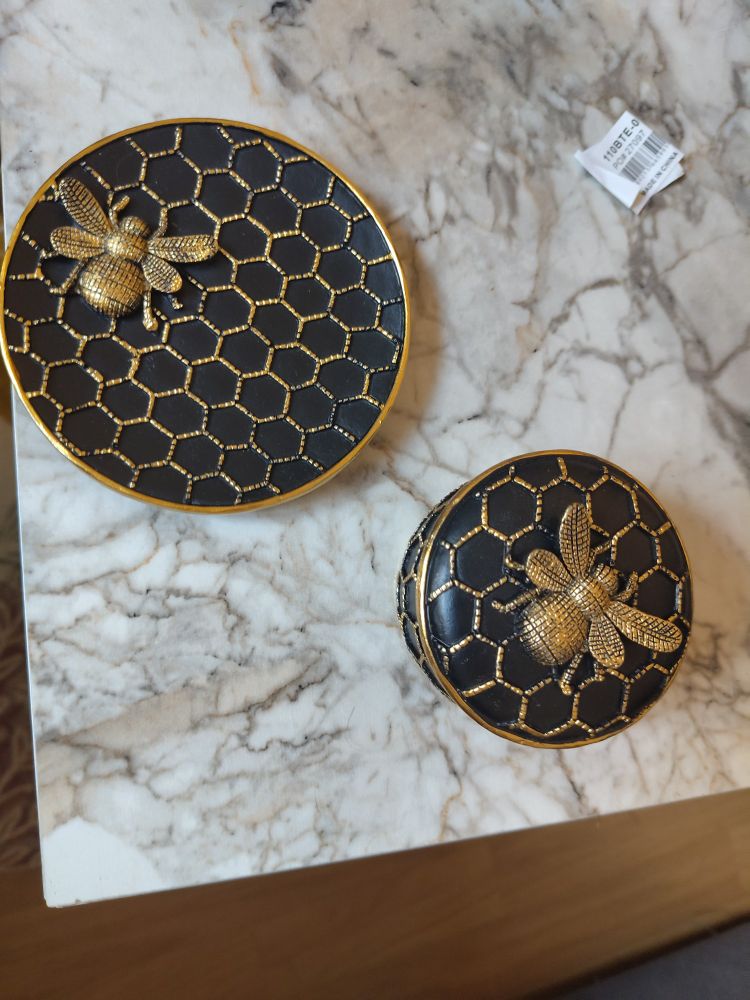 Assiette et boîte noire avec une abeille dorée représentée dessus et des dessins d'alvéoles dorés également 