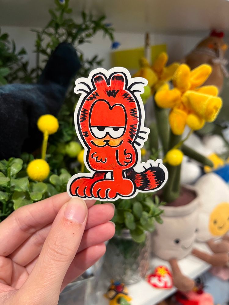 A picture of a hand holding up a Garfield sticker