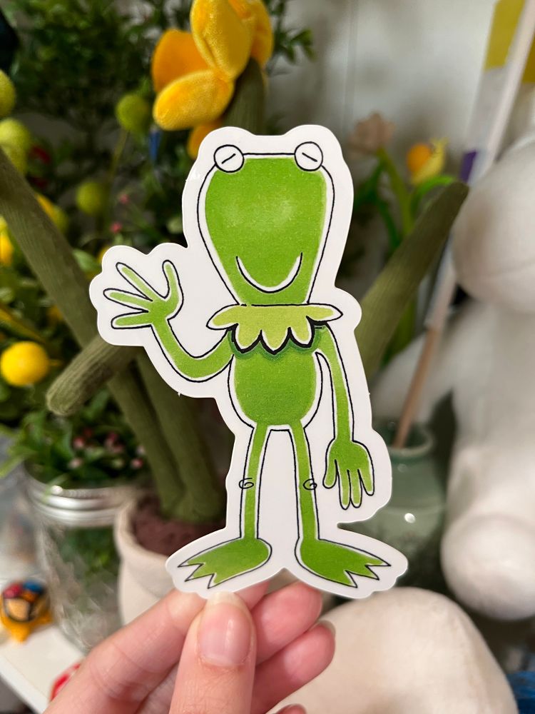 A photo of a hand holding up a Kermit sticker 