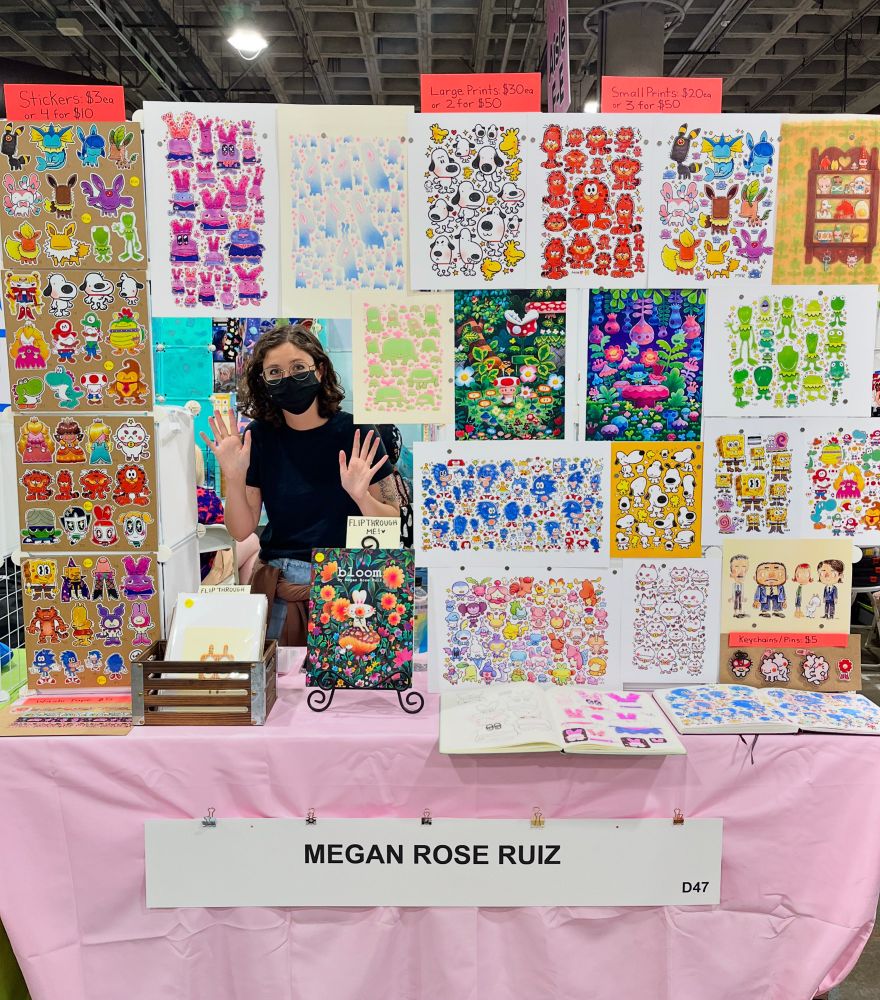A photo of me standing behind my table and display of artwork at Anime Expo