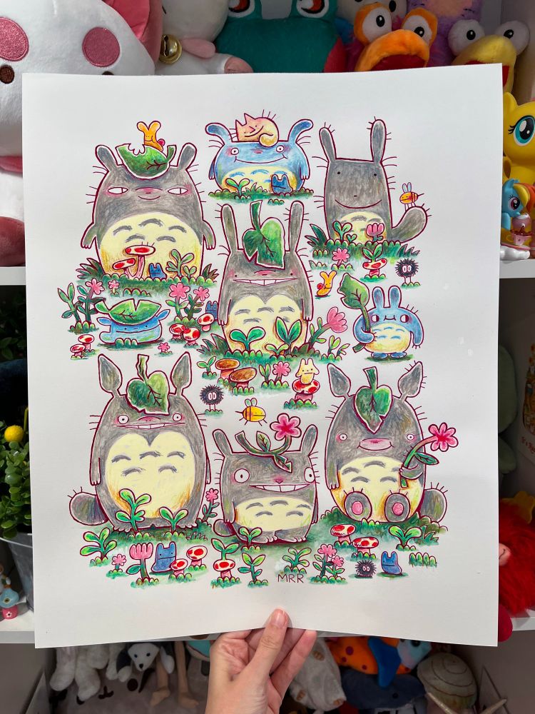 A picture of a hand holding up a piece of paper with an illustration of Totoro! There are 9 different Totoro drawings in the illustration. 