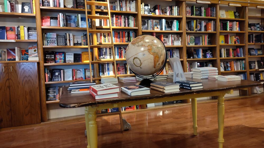 Bookstore shelves to the ceiling. A table with books and a world globe.
