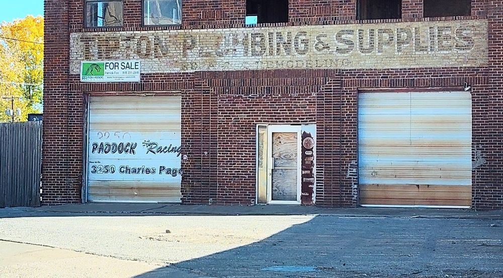 A shuttered red brick building with a ghost sign, Tipton Plumbing & Supplies 