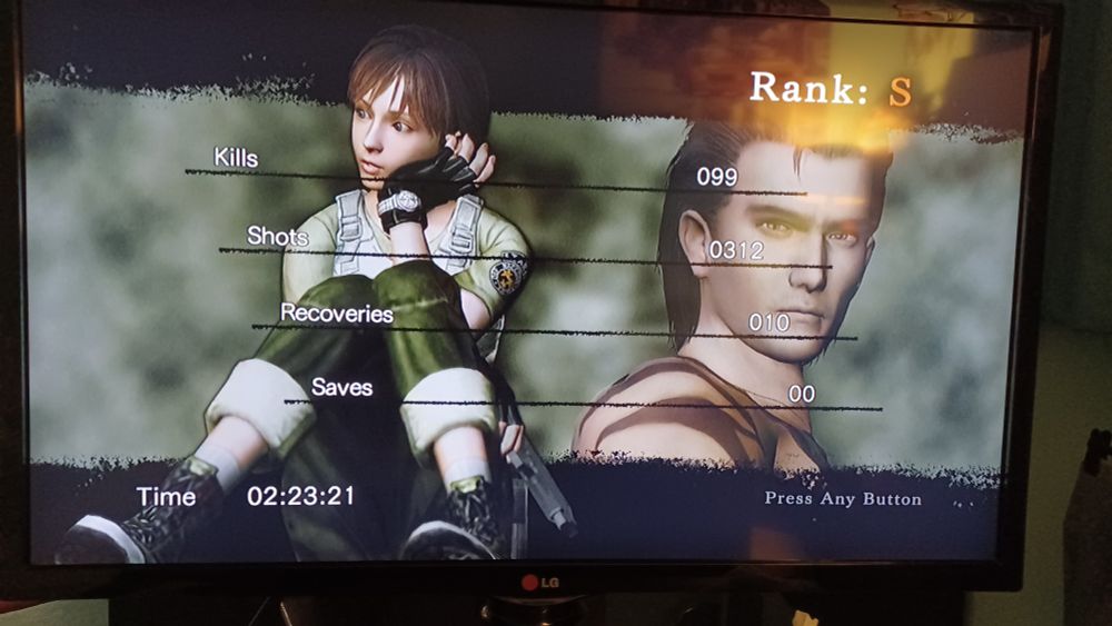 A photo of a TV screen, which shows the "game complete" card that appears at the end of a successful Resident Evil Zero playthrough. This player has earned an S Rank, the best possible ranking, having completed the game in a mere 2 hours, 23 minutes, and 21 seconds. The player had 99 kills, took 312 shots, used 10 recovery items, and beat the game without saving once.