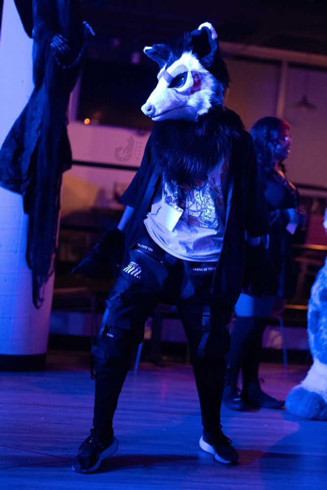 a neon blue and purple photograph of a person wearing a possum partial fursuit while dancing.