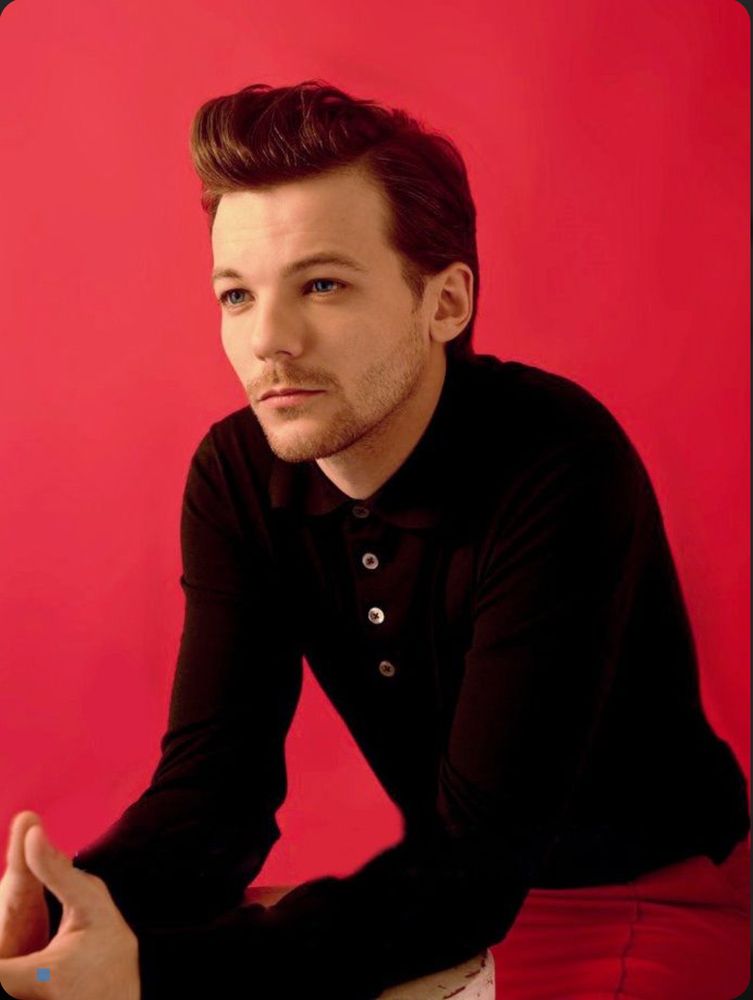 Louis Tomlinson in a black shirt. His hair is in a quiff. 