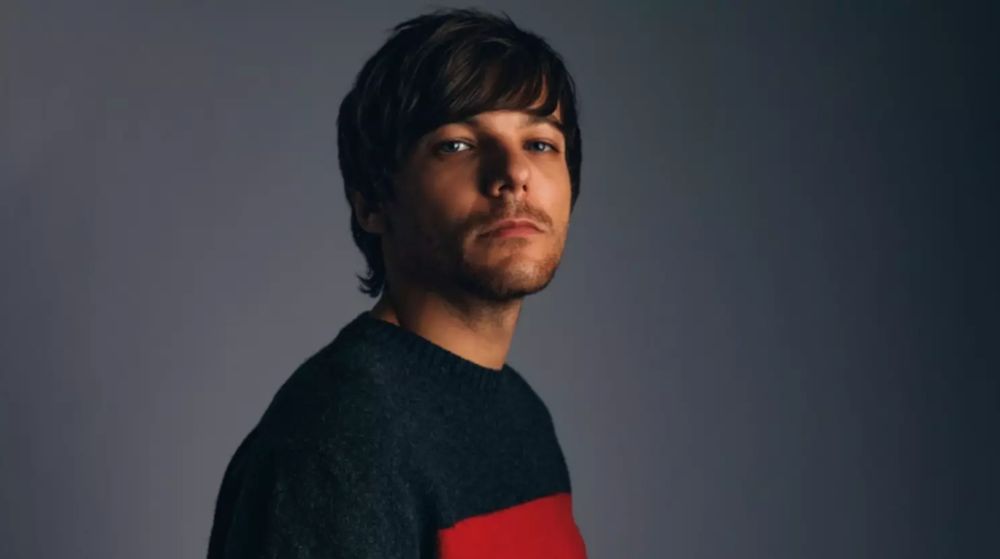 Portrait of Louis Tomlinson in a charcoal and red sweater against a moody grey background