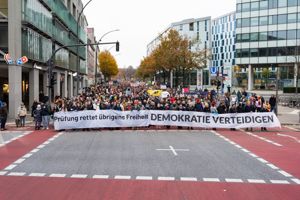 Demomenge mit Transparenten, auf denen der Text “Prüfung rettet übrigens Freiheit” und “DEMOKRATIE VERTEIDIGEN” steht.