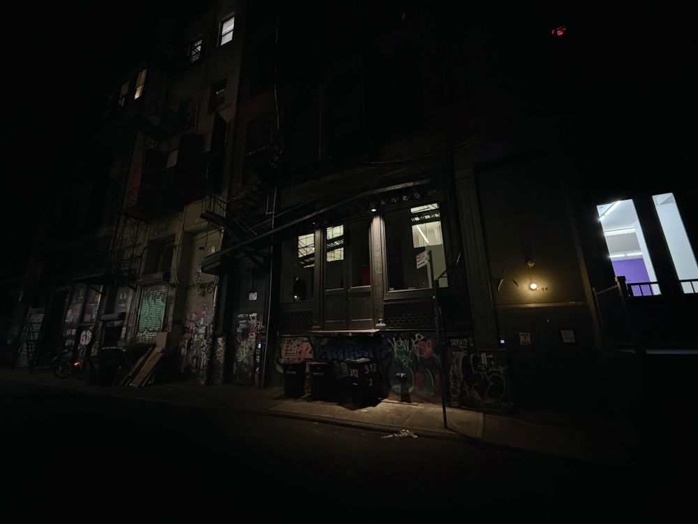 A nighttime photo of a back alley in Tribeca, New York. The darkness is broken by a handful of windows and an unseen source of light coming from the left. Truly urban, graffiti, desolate - Tribeca Noir.