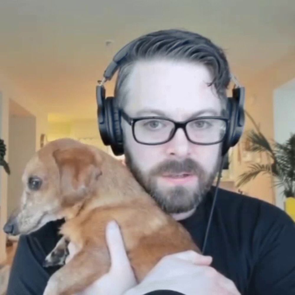 a man wearing glasses and headphones holds a small dog