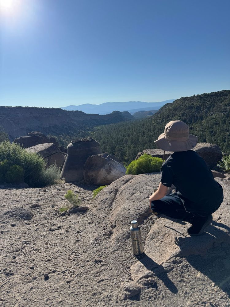 An 8 year old boy crouches and looks down a canyon at the Sangre de Cristos mountains in the distance 