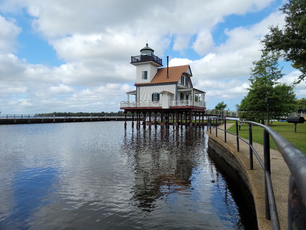 A lighthouse on stilts next to a riverfront park.