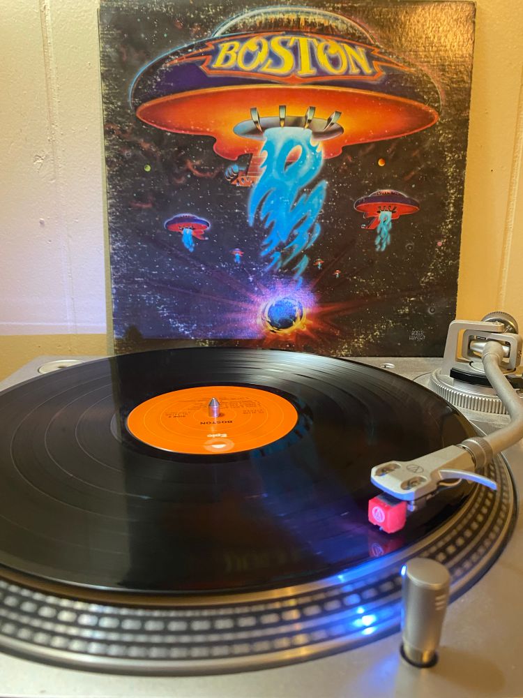 lp cover of the self titled debut from Boston (1976), it’s several acoustic guitars but like, they’re spaceships man. a good amount of ring wear. orange epic label on the record on the turntable 