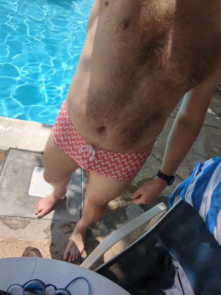 A dude wearing a pink swim sunga standing in front of a pool 