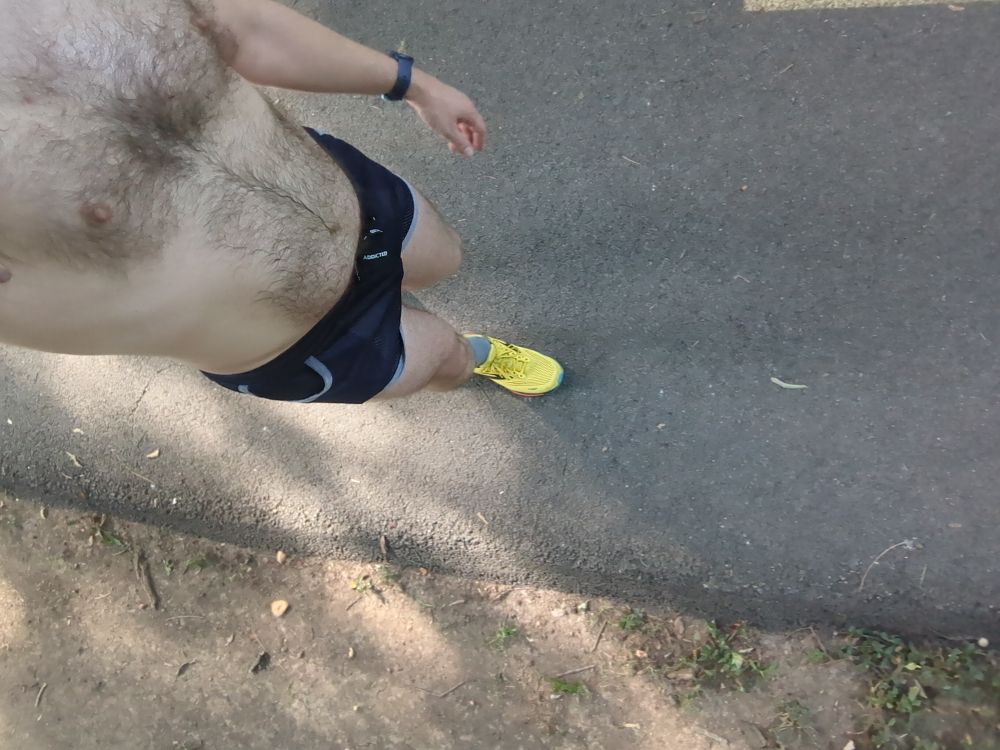 A dude wearing a pair of blue running shorts and yellow running shoes walking on a bike trail 
