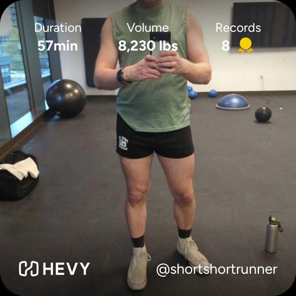 A dude wearing a pair of black gym shorts, green muscle shirt and white Chucks taking a selfie in the mirror of a gym studio 